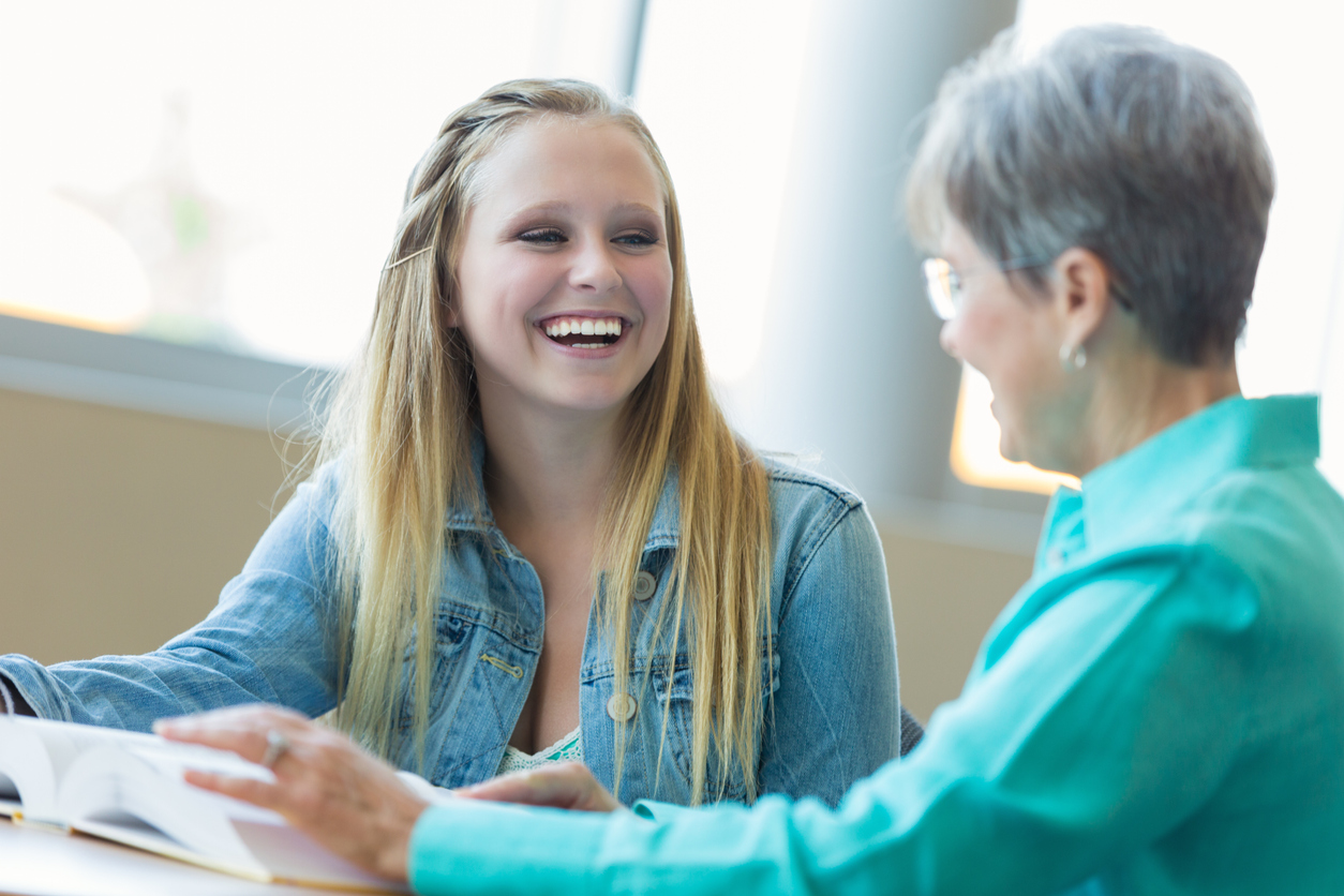 Teenage girl laughs with teacher in school library